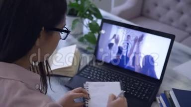 电子培训，戴眼镜的女生在笔记本上看视频时用钢笔在笔记本上写字